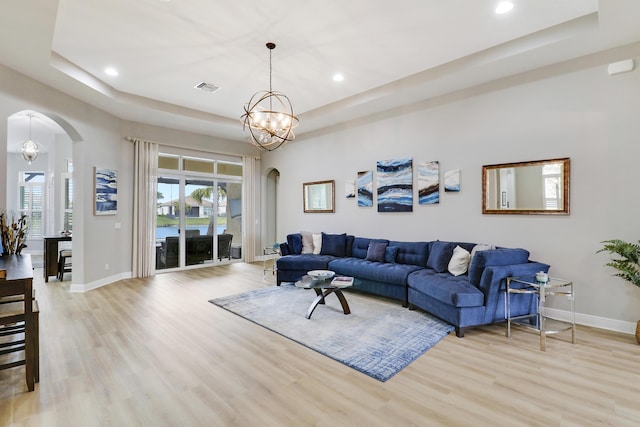 living room with a raised ceiling, light wood-type flooring, and an inviting chandelier