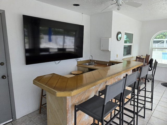 kitchen with kitchen peninsula, light tile patterned flooring, a breakfast bar area, and sink