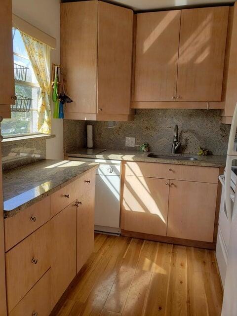 kitchen with dishwasher, light hardwood / wood-style floors, light stone countertops, and sink