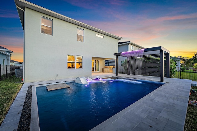 pool at dusk with pool water feature, a patio, and an outdoor kitchen