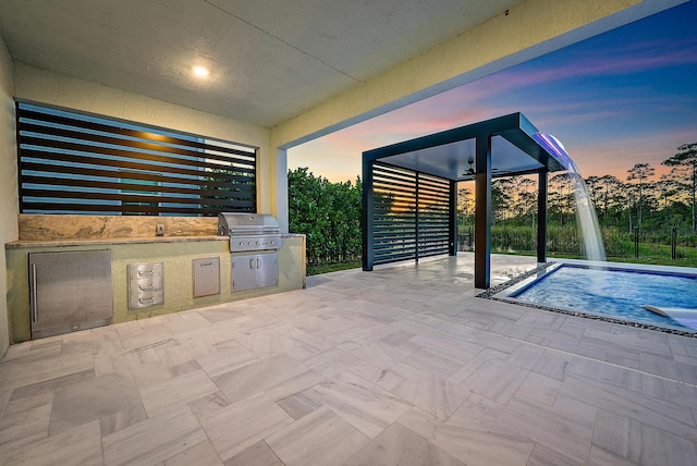 patio terrace at dusk with a fenced in pool, grilling area, pool water feature, and an outdoor kitchen