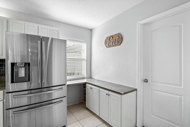 kitchen featuring stainless steel fridge, a textured ceiling, white cabinetry, and light tile patterned flooring