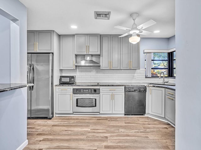 kitchen featuring sink, wall chimney range hood, stainless steel appliances, and light wood-type flooring