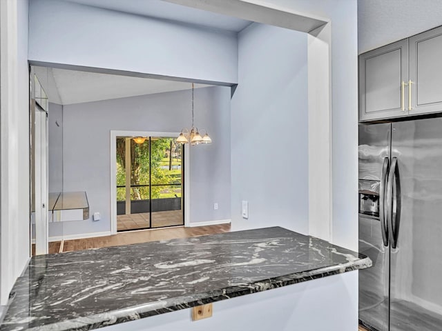 kitchen featuring gray cabinetry, stainless steel fridge, dark stone counters, and a notable chandelier