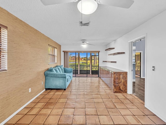 interior space with a textured ceiling, ceiling fan, wooden walls, and light tile patterned flooring