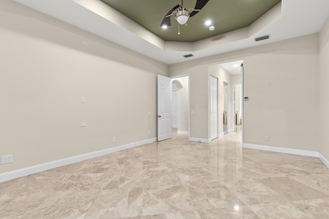 empty room with ceiling fan and a tray ceiling