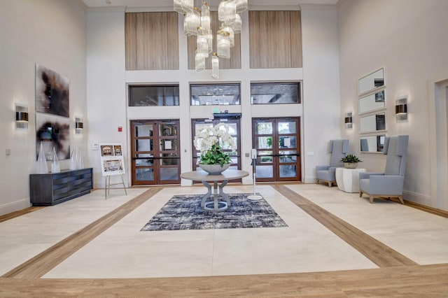 foyer entrance with light hardwood / wood-style floors, a towering ceiling, an inviting chandelier, and french doors