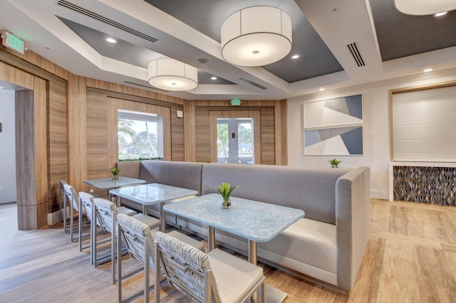 dining room featuring a tray ceiling, light hardwood / wood-style flooring, and wood walls