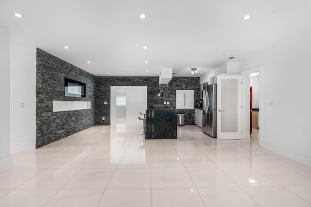 kitchen featuring a kitchen bar, stainless steel fridge, white cabinetry, and light tile patterned flooring