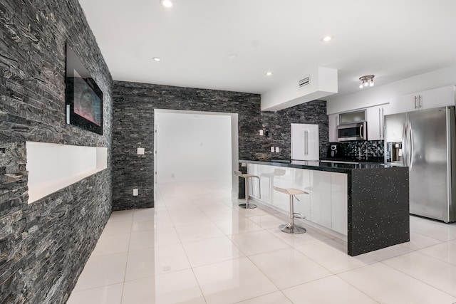 kitchen with a breakfast bar area, light tile patterned floors, a kitchen island, white cabinetry, and stainless steel appliances