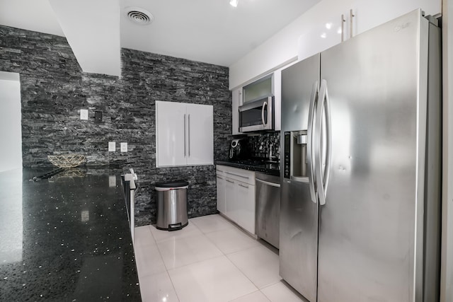 kitchen with backsplash, white cabinets, tile walls, light tile patterned flooring, and stainless steel appliances