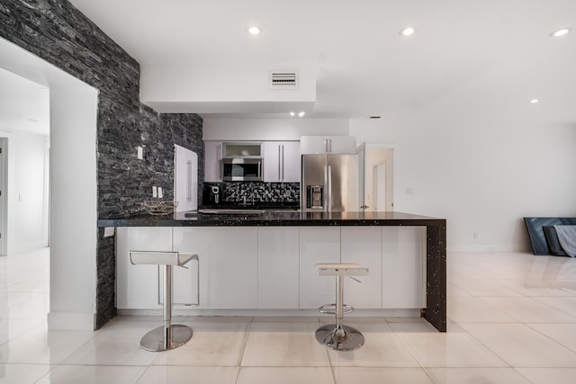 kitchen featuring white cabinets, light tile patterned floors, appliances with stainless steel finishes, kitchen peninsula, and a breakfast bar area