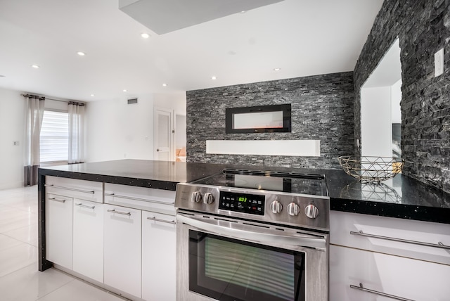 kitchen featuring light tile patterned floors, backsplash, dark stone counters, stainless steel electric stove, and white cabinets