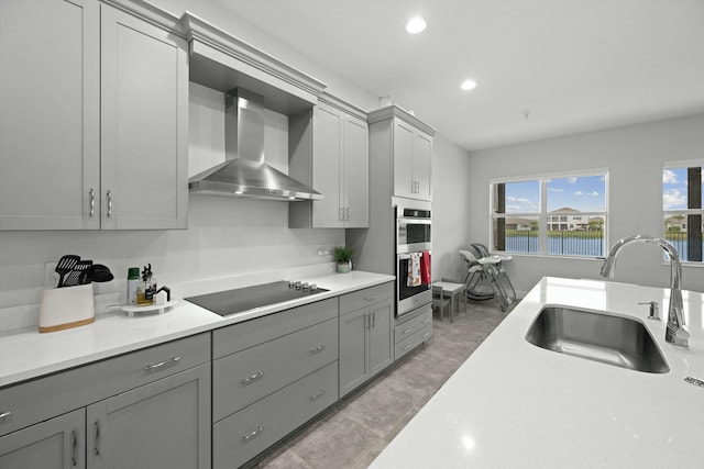 kitchen with black electric stovetop, light countertops, gray cabinetry, a sink, and wall chimney exhaust hood