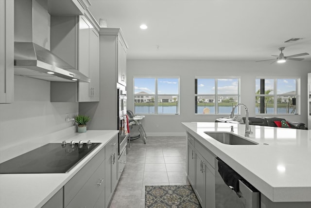 kitchen featuring light countertops, black electric cooktop, stainless steel dishwasher, wall chimney range hood, and a sink