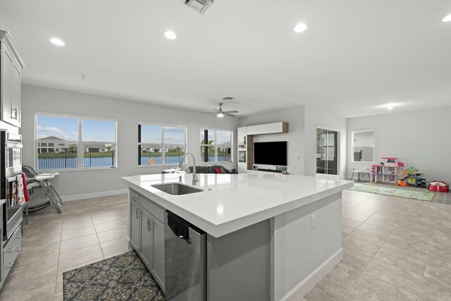 kitchen with appliances with stainless steel finishes, gray cabinetry, a kitchen island with sink, a kitchen breakfast bar, and wall chimney exhaust hood