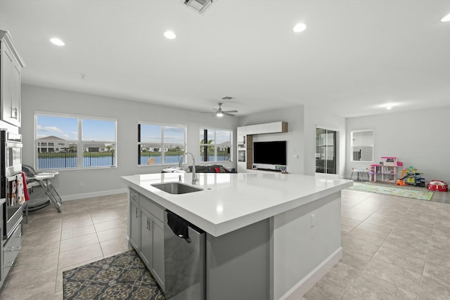 kitchen featuring a sink, open floor plan, light countertops, appliances with stainless steel finishes, and a center island with sink