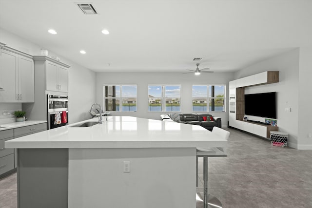 kitchen with a kitchen island with sink, open floor plan, a sink, and gray cabinetry