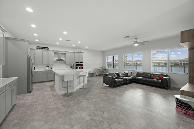 kitchen featuring a breakfast bar, a water view, gray cabinets, an island with sink, and wall chimney range hood