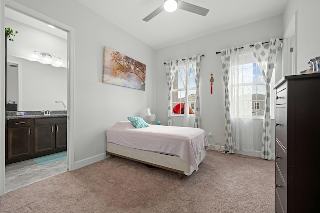 bedroom featuring a ceiling fan, baseboards, light carpet, and ensuite bath