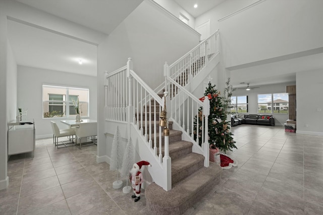 stairway featuring a towering ceiling, tile patterned flooring, baseboards, and ceiling fan