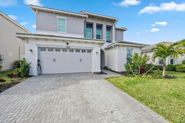 view of front of home with decorative driveway, an attached garage, a front lawn, and stucco siding