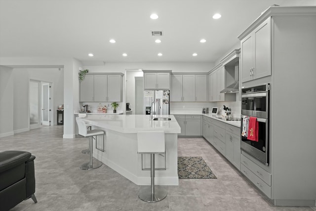 kitchen featuring an island with sink, stainless steel appliances, gray cabinets, light countertops, and a kitchen bar