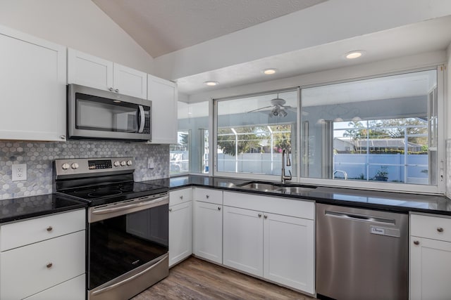 kitchen with white cabinetry, sink, stainless steel appliances, vaulted ceiling, and decorative backsplash