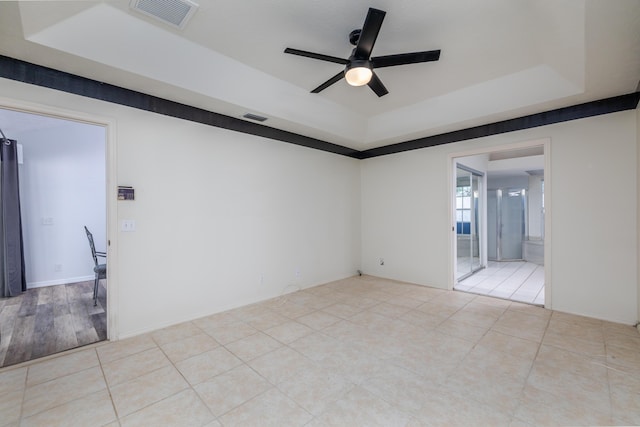 tiled empty room with a raised ceiling and ceiling fan