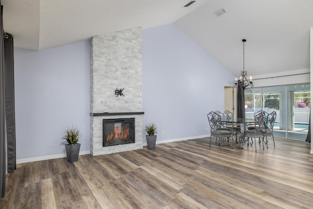 dining space with a stone fireplace, hardwood / wood-style floors, high vaulted ceiling, and a chandelier