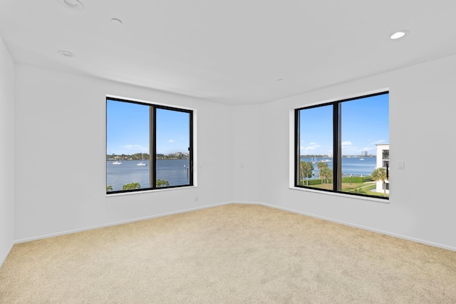 unfurnished room featuring a water view and light colored carpet