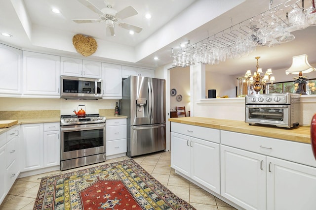 kitchen featuring stainless steel appliances, white cabinetry, hanging light fixtures, and butcher block countertops