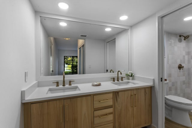 bathroom with tiled shower, vanity, and toilet