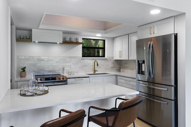 kitchen with a breakfast bar, white cabinets, a raised ceiling, sink, and stainless steel appliances