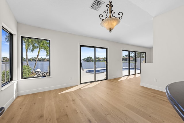 unfurnished room with a wealth of natural light, a water view, and light hardwood / wood-style floors