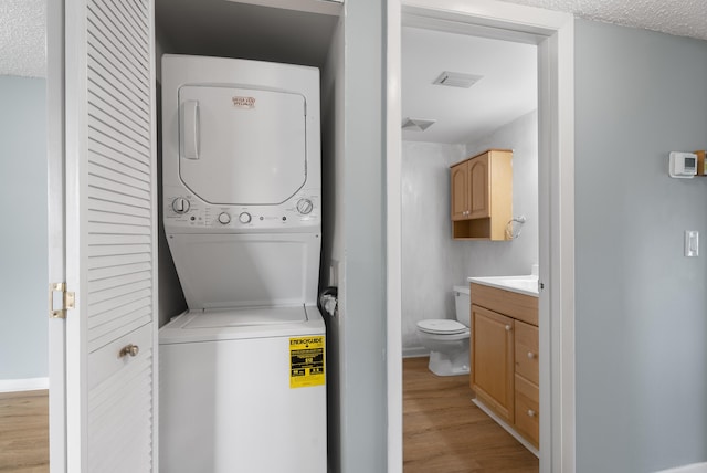 151 SW S River Dr Unit 203, Stuart, FL 34997 - washroom featuring estacked washer and dryer, light wood-style floors, and a textured ceiling