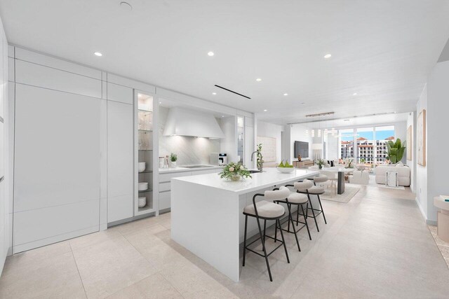 kitchen with a large island, sink, a breakfast bar area, white cabinets, and custom exhaust hood