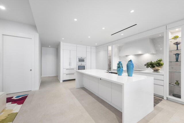 kitchen featuring white cabinetry, sink, stovetop, a center island with sink, and custom exhaust hood