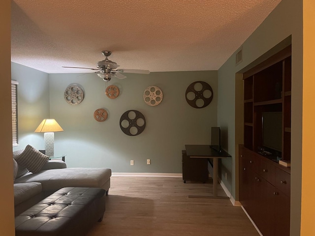 living room with a textured ceiling, ceiling fan, built in features, and light hardwood / wood-style floors