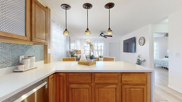 kitchen featuring stainless steel dishwasher, kitchen peninsula, light hardwood / wood-style floors, decorative light fixtures, and decorative backsplash