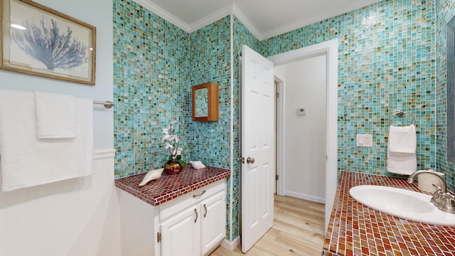 bathroom with crown molding, sink, wood-type flooring, and tile walls