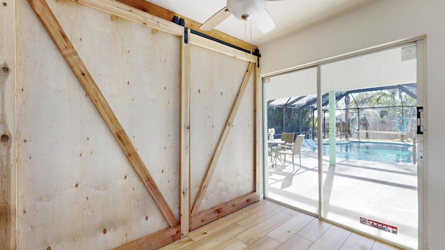 doorway with light wood-type flooring, a barn door, and ceiling fan