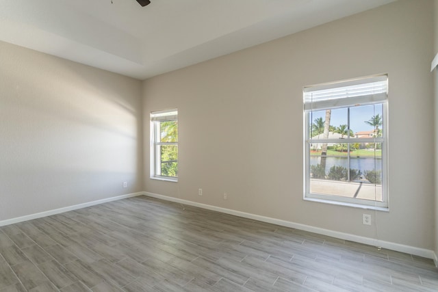 empty room featuring ceiling fan, a water view, wood finished floors, and baseboards