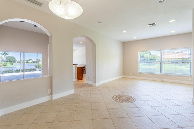 empty room featuring light tile patterned floors, visible vents, and a healthy amount of sunlight