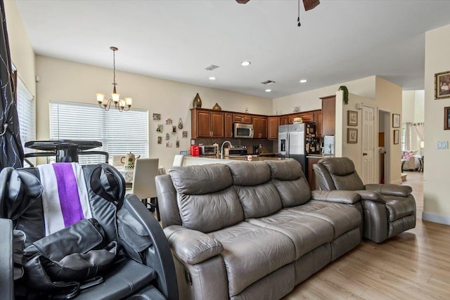 living room featuring ceiling fan with notable chandelier and light wood-type flooring