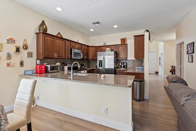 kitchen featuring kitchen peninsula, appliances with stainless steel finishes, backsplash, light stone counters, and sink