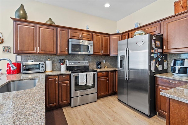 kitchen featuring sink, light stone counters, light hardwood / wood-style flooring, backsplash, and appliances with stainless steel finishes