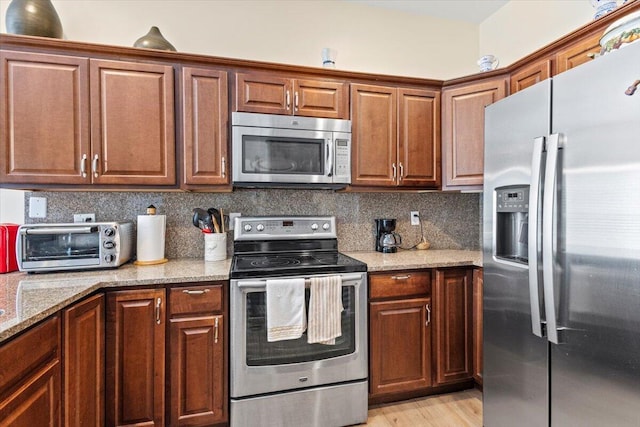 kitchen featuring tasteful backsplash, light stone countertops, light wood-type flooring, and appliances with stainless steel finishes