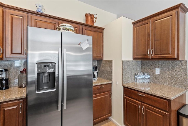 kitchen with tasteful backsplash, stainless steel fridge with ice dispenser, and light stone countertops