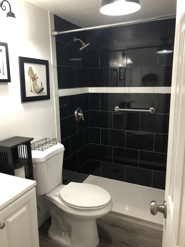 bathroom featuring toilet, hardwood / wood-style floors, vanity, and tiled shower